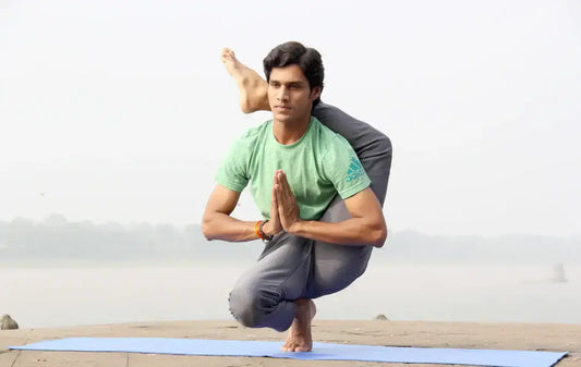 Man practicing yoga on a mat while wearing a green t-shirt, showcasing balance and flexibility outdoors.