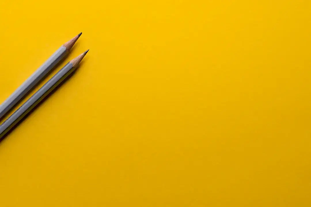 Two pencils on bright yellow background representing creativity and art design.