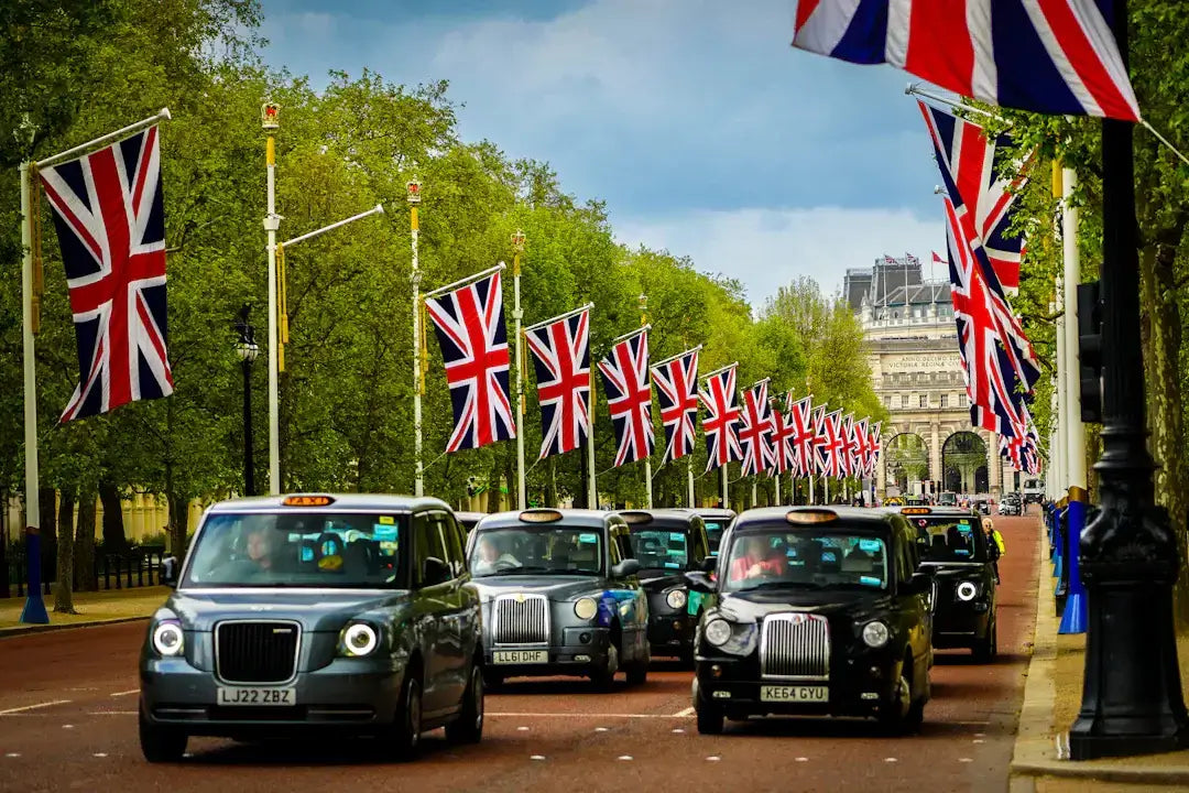 London black cabs driving down a street lined with Union Jack flags.