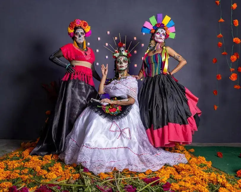 Three women in vibrant traditional Mexican costumes with colorful patterns and makeup, surrounded by marigold flowers.