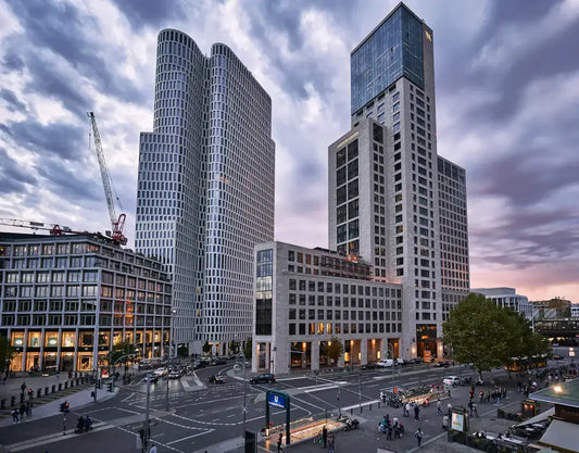 Modern cityscape with tall skyscrapers and bustling streets at a crossroads, showcasing urban architecture and evening sky.