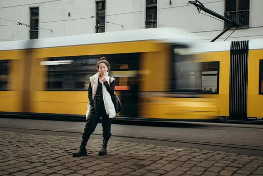 Woman in streetwear outfit standing by a motion-blurred yellow tram, reflecting urban style and dynamic street culture.