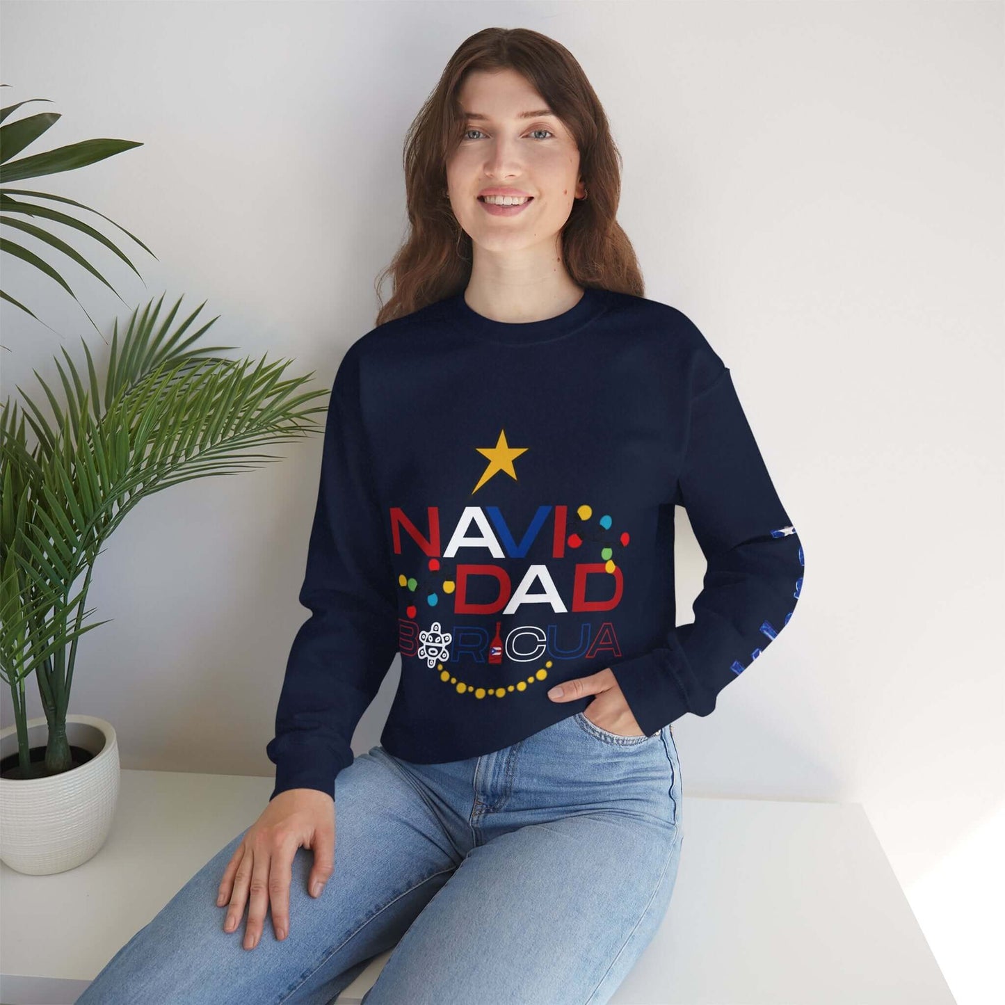 Woman wearing a customizable black Christmas sweater with vibrant "NAVIDAD BORICUA" design, festive sleeve print, sitting indoors.