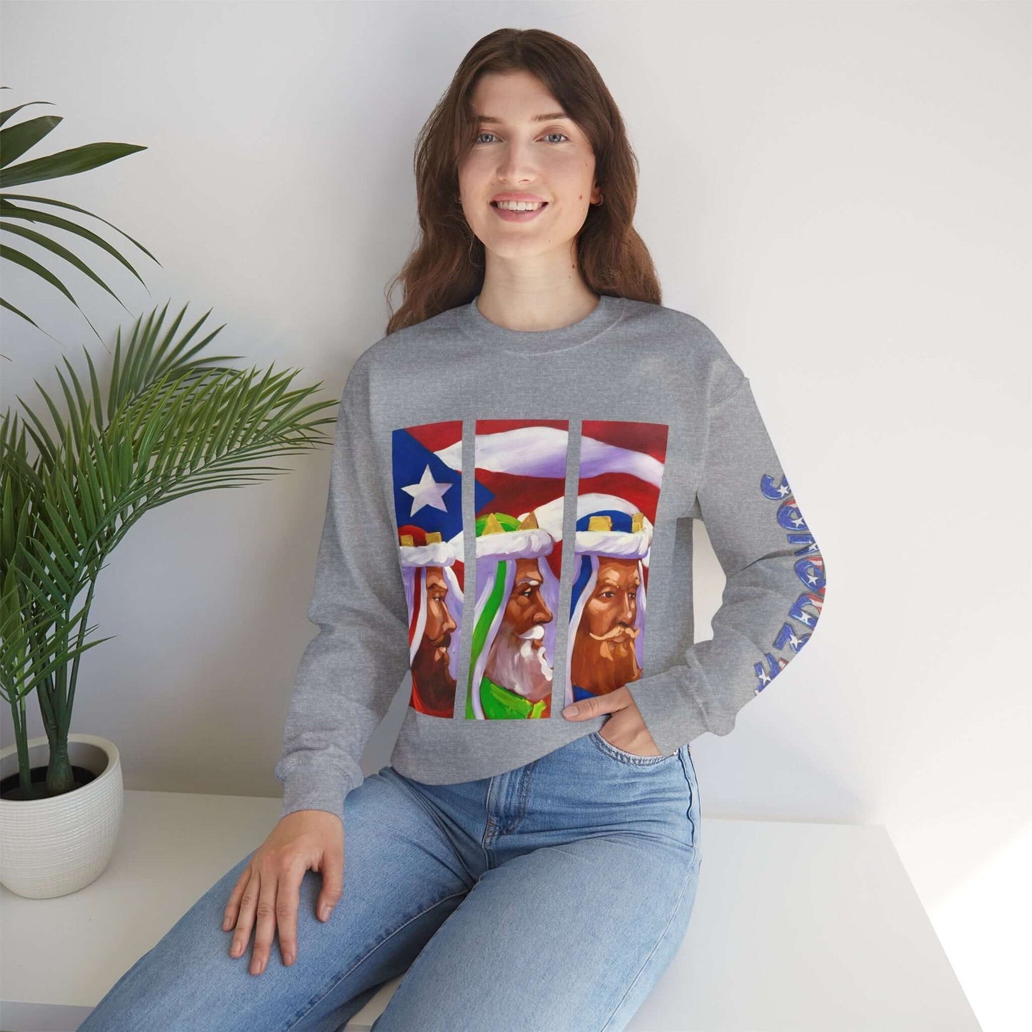 Woman modeling a festive sweater with Three Kings and Puerto Rican flag design, sitting on a chair next to a potted plant.